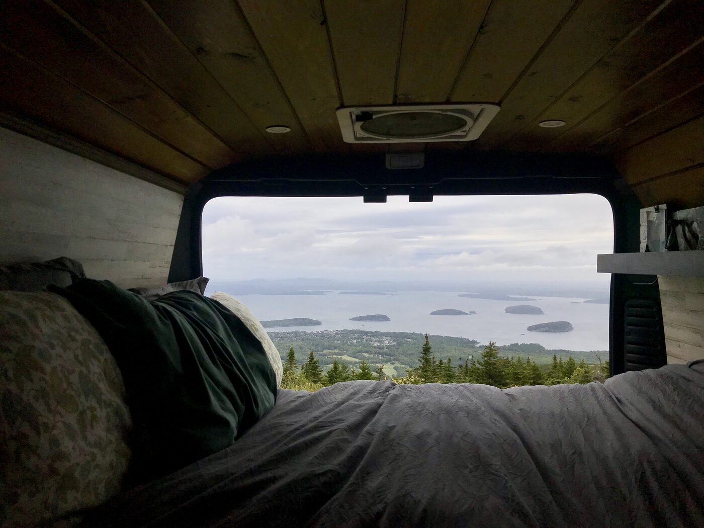 The view from the van's bed through open rear doors, islands scattered across the water below