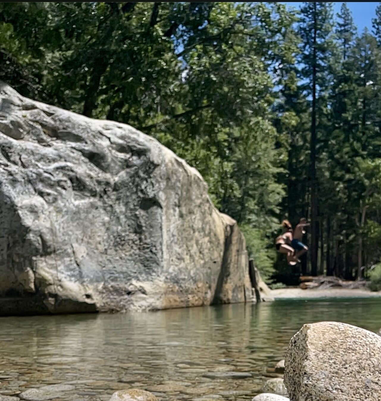 A wide granite boulder above a clear river with people swimming below