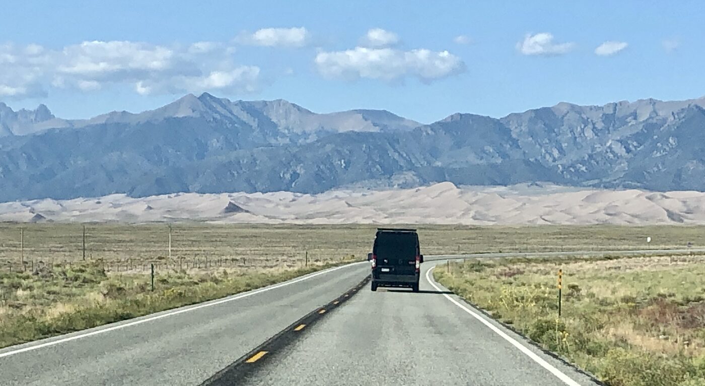 The van alone on a straight two-lane highway, dunes and mountains ahead