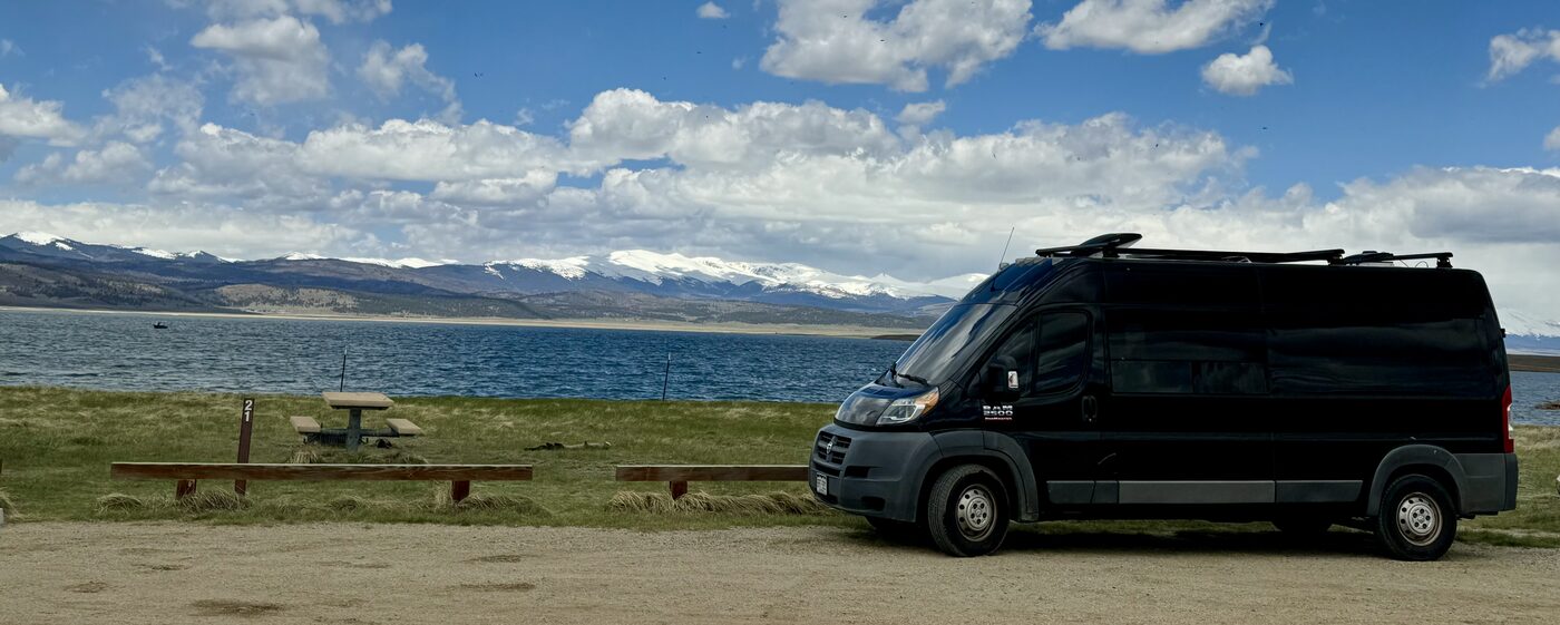 The van parked beside an alpine lake with snow-capped mountains behind