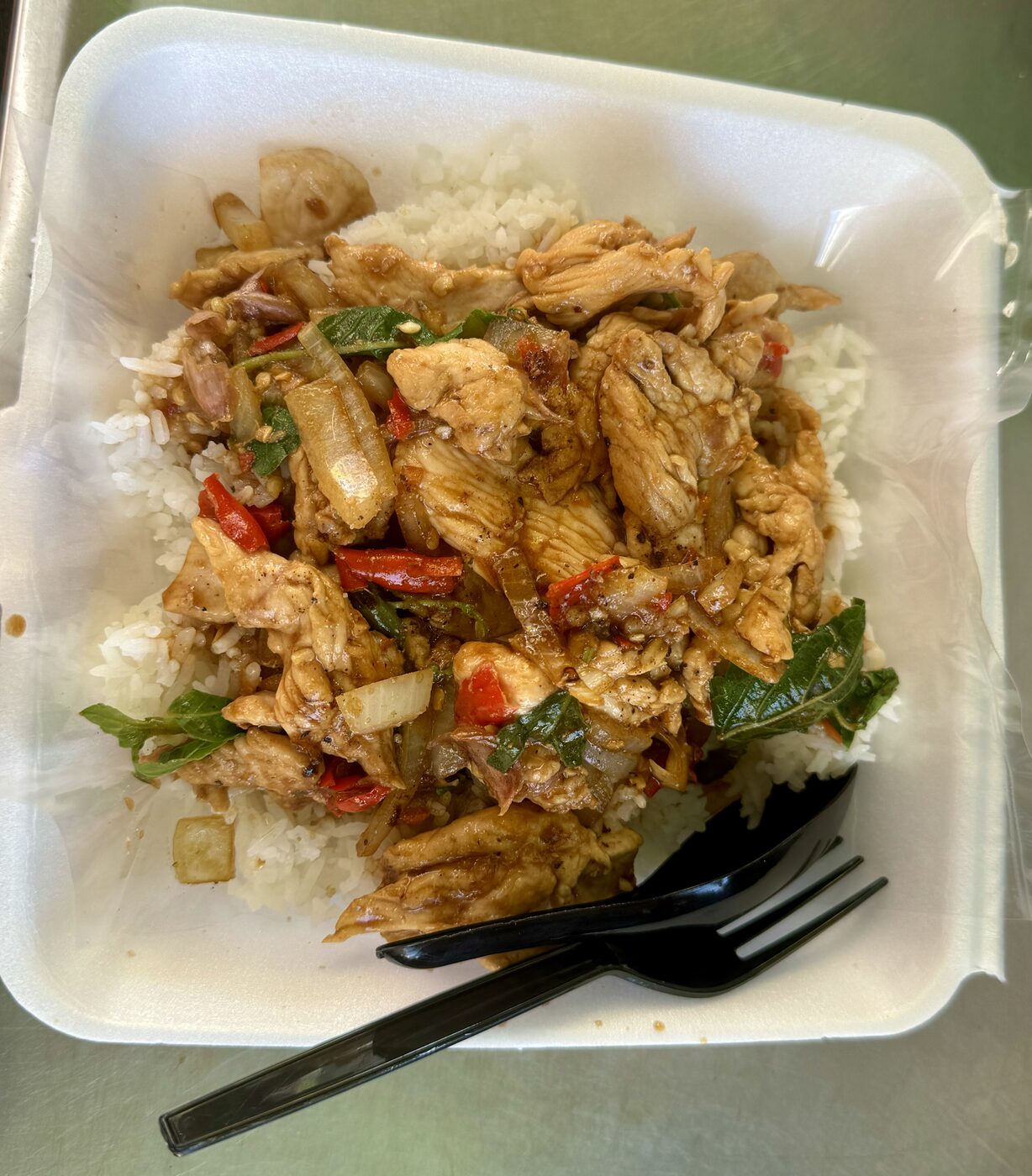 A styrofoam container of pad krapow over rice from a street cart