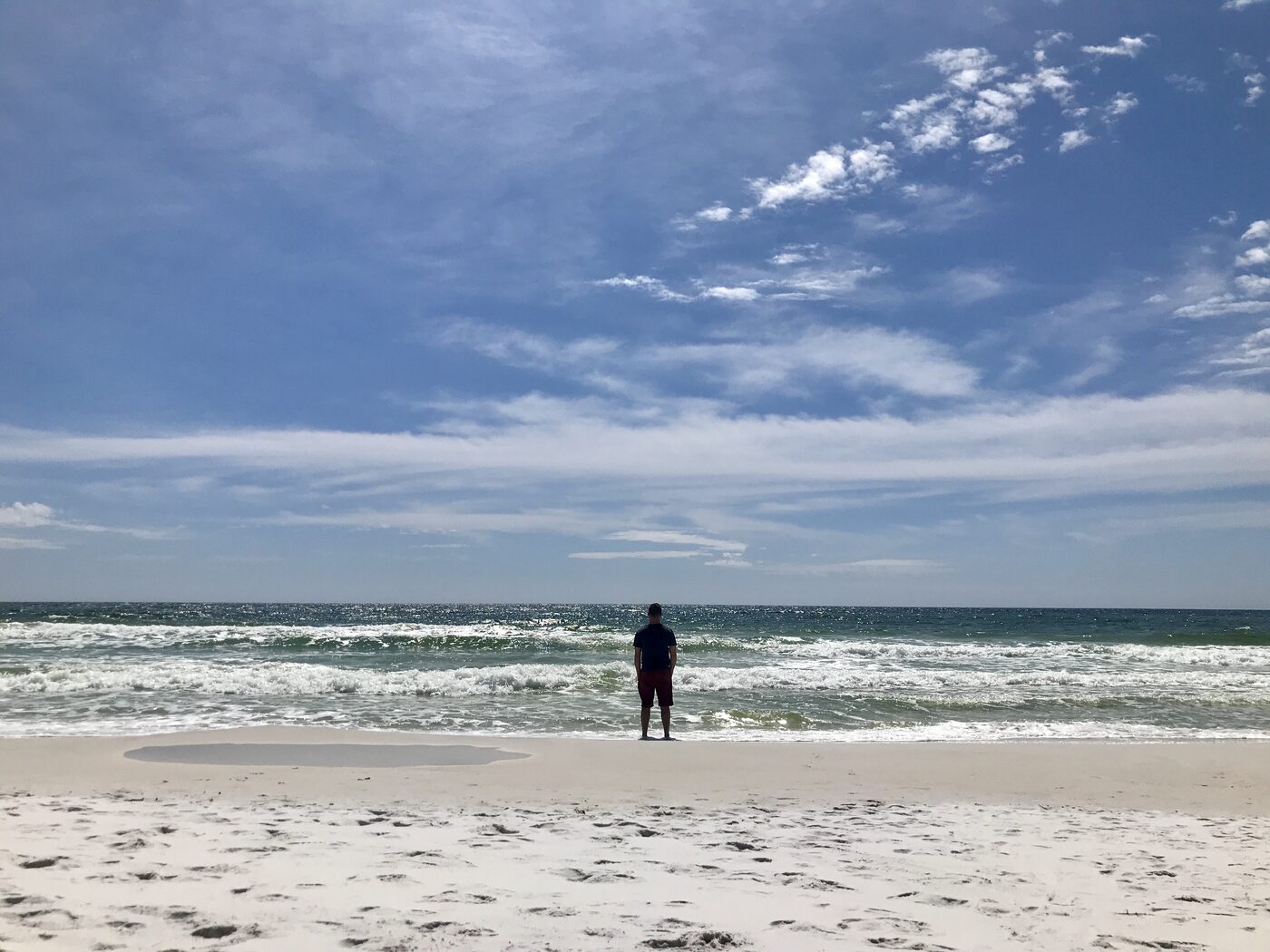 Jesse standing alone at the edge of the Gulf on the white sand of Santa Rosa Beach