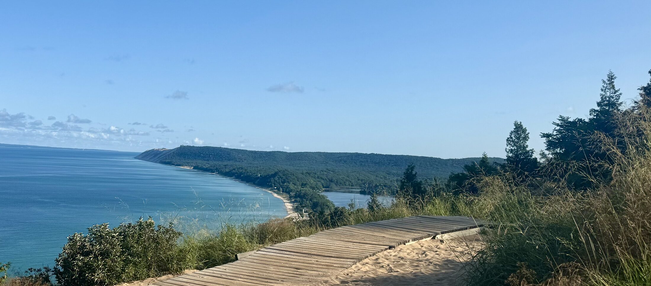 A sand and boardwalk path along a dune bluff, Lake Michigan stretching away to a wooded headland