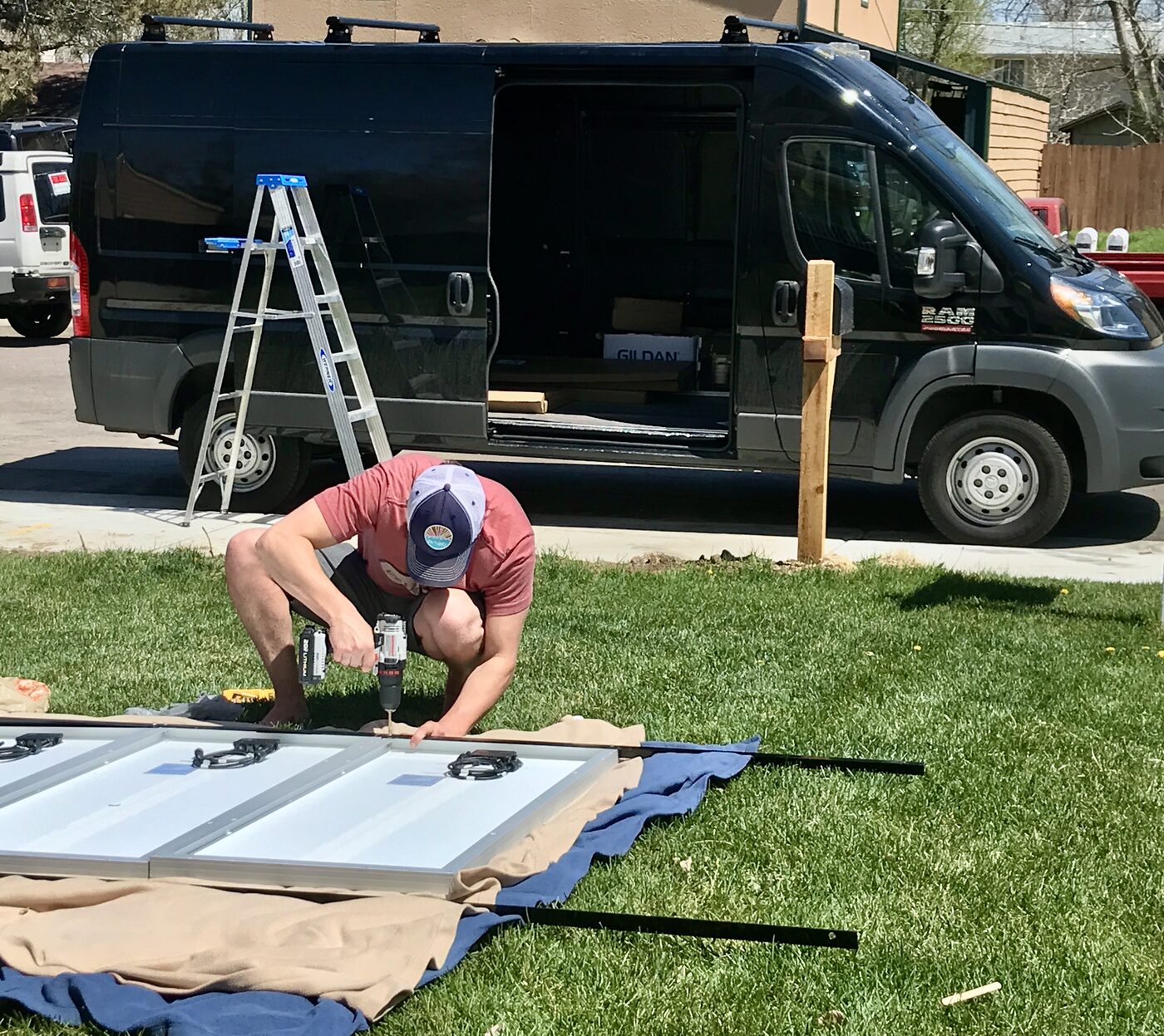 Jesse drilling panels on the lawn beside the van mid-build